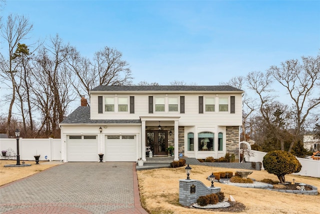 traditional home featuring a chimney, an attached garage, fence, stone siding, and driveway