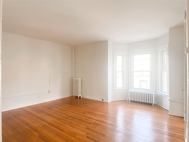 unfurnished room with radiator heating unit, light wood-type flooring, and baseboards