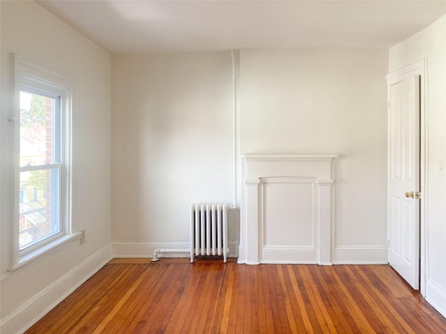 unfurnished room featuring baseboards, hardwood / wood-style floors, and radiator