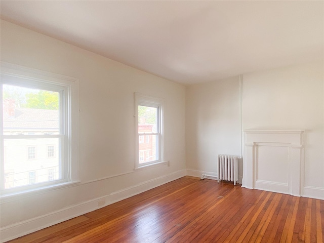 empty room featuring radiator heating unit, baseboards, and hardwood / wood-style floors