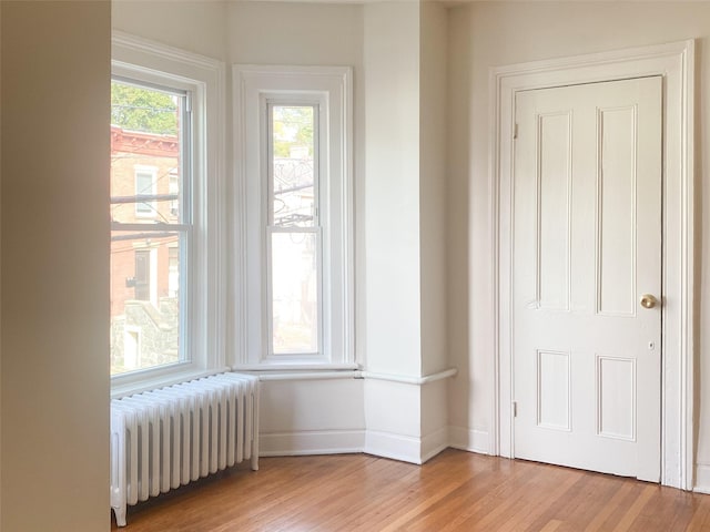 empty room with radiator, light wood-style flooring, and baseboards