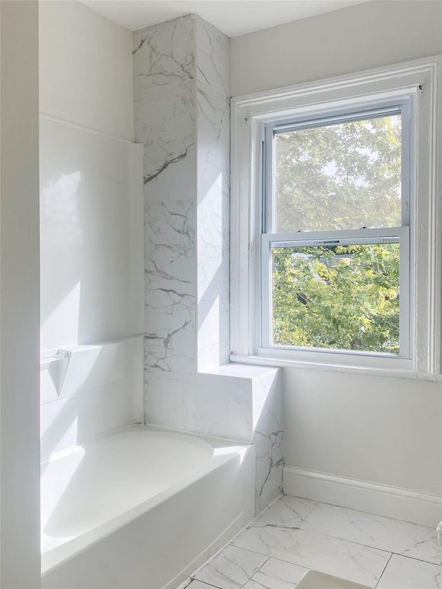 bathroom with marble finish floor, baseboards, and a bath