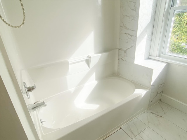 bathroom with marble finish floor, baseboards, and a bathtub