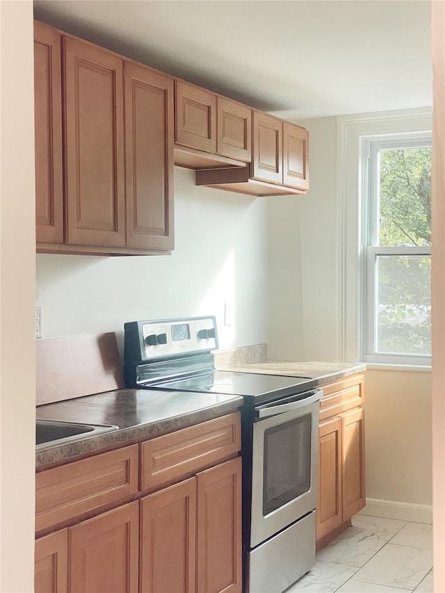 kitchen with marble finish floor, a sink, stainless steel range with electric stovetop, and baseboards