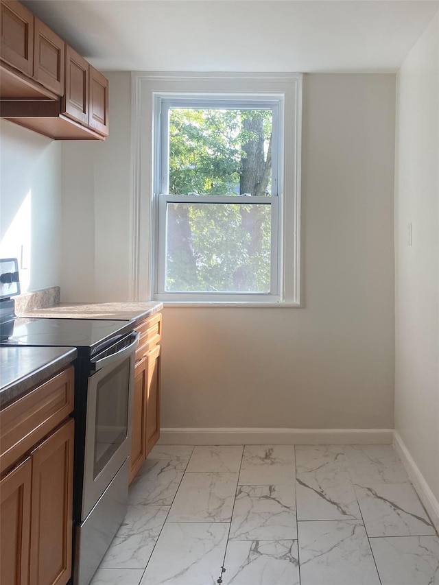 kitchen with marble finish floor, electric range, baseboards, and brown cabinets