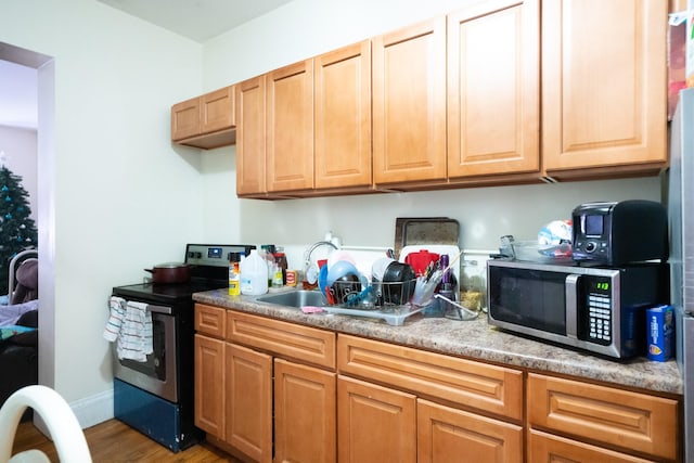 kitchen with light countertops, appliances with stainless steel finishes, a sink, wood finished floors, and baseboards