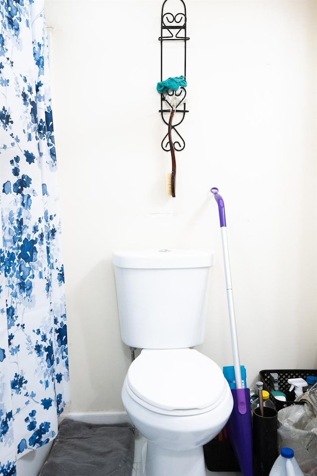 bathroom featuring a shower with shower curtain, toilet, and baseboards