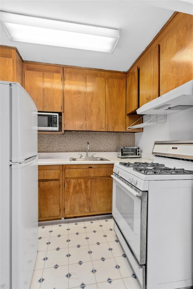 kitchen featuring white appliances, brown cabinetry, light countertops, under cabinet range hood, and a sink