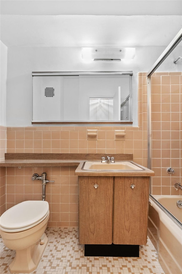 bathroom featuring toilet, bath / shower combo with glass door, vanity, and tile walls