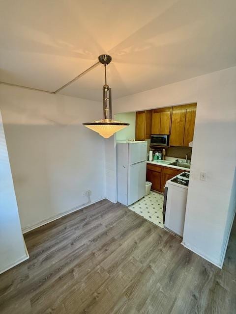 kitchen with brown cabinets, light countertops, hanging light fixtures, wood finished floors, and white appliances