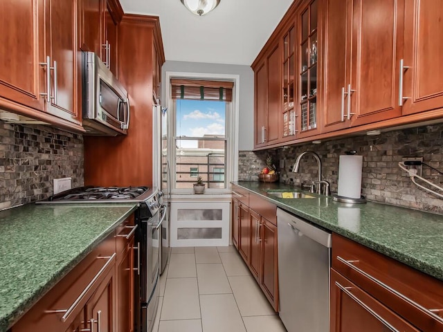 kitchen featuring light tile patterned floors, tasteful backsplash, glass insert cabinets, stainless steel appliances, and a sink