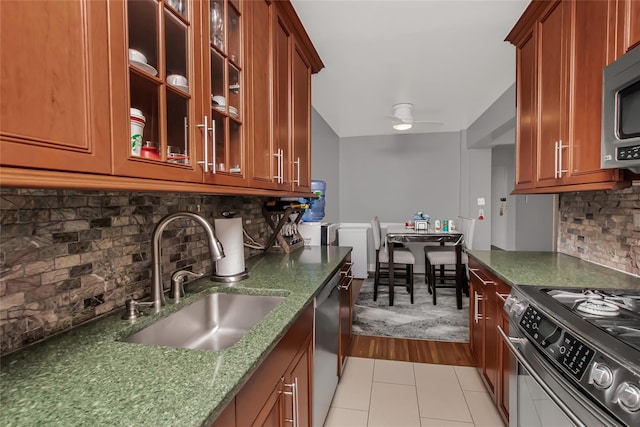 kitchen featuring decorative backsplash, appliances with stainless steel finishes, a ceiling fan, a sink, and dark stone counters