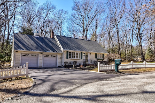 view of front of house featuring a garage, roof with shingles, aphalt driveway, and a fenced front yard