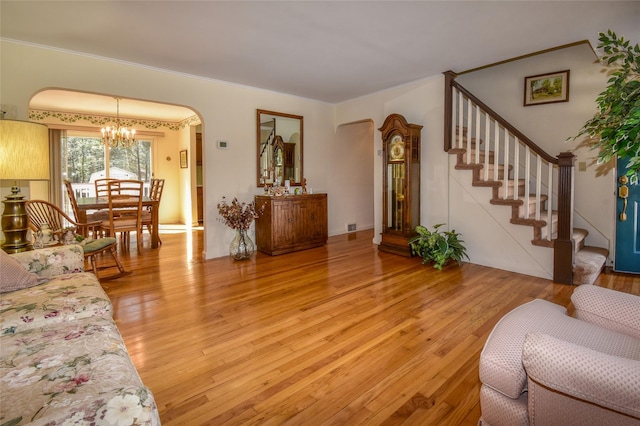 living room with ornamental molding, a chandelier, light wood-style flooring, and stairs