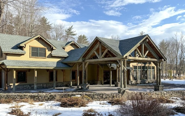 view of front of home with stone siding, covered porch, and roof with shingles