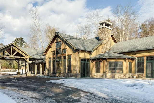 view of front of property with stone siding, a chimney, and roof with shingles