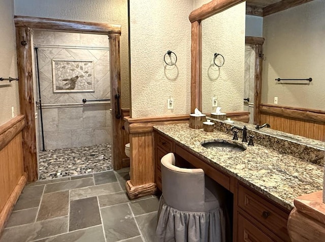 bathroom featuring toilet, stone tile floors, vanity, wainscoting, and a stall shower