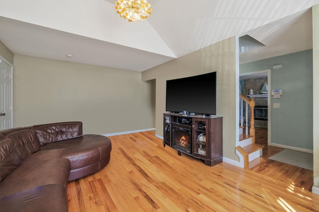 living room featuring a glass covered fireplace, wood finished floors, a chandelier, baseboards, and stairs