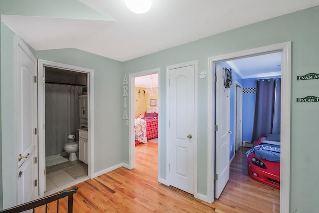 corridor featuring light wood-style floors, baseboards, and vaulted ceiling