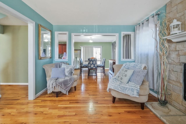 sitting room featuring light wood-type flooring, a stone fireplace, and baseboards