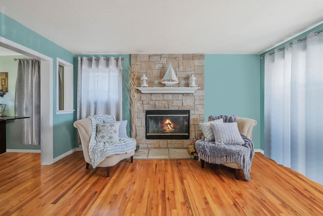 living area featuring a stone fireplace, baseboards, and wood finished floors