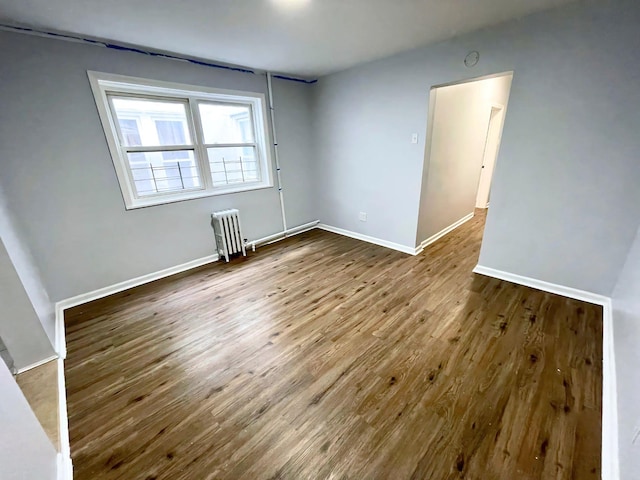 unfurnished room featuring baseboards, wood finished floors, and radiator