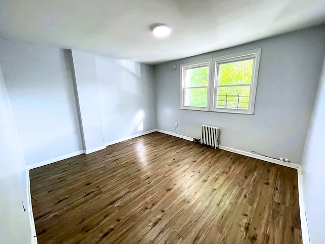 spare room featuring radiator heating unit, dark wood finished floors, and baseboards