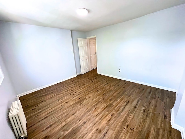 spare room featuring radiator heating unit, baseboards, and wood finished floors