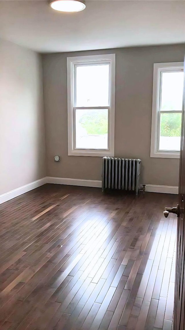 spare room with baseboards, dark wood finished floors, and radiator heating unit