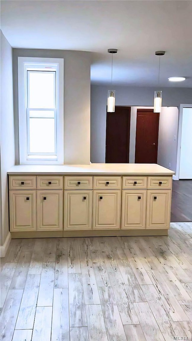 kitchen with light wood-type flooring, light countertops, hanging light fixtures, and cream cabinets