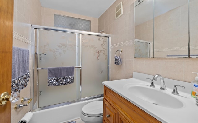 full bath with tile walls, bath / shower combo with glass door, visible vents, toilet, and vanity