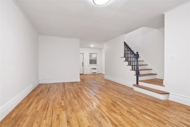 unfurnished room featuring light wood-style floors, radiator, stairway, and baseboards