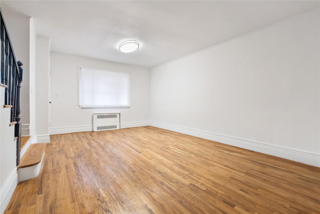 empty room with heating unit, stairway, baseboards, and wood finished floors