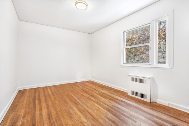 empty room with radiator heating unit, baseboards, and light wood-style flooring