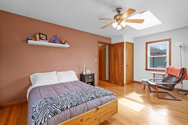 bedroom with ceiling fan, a skylight, light wood-style flooring, and baseboards