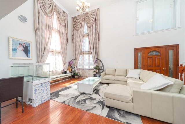 living room with a chandelier, ornamental molding, a high ceiling, and wood finished floors