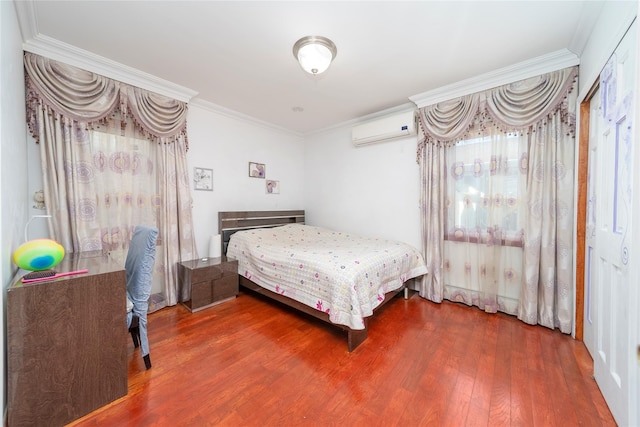 bedroom with ornamental molding, a wall unit AC, and wood finished floors