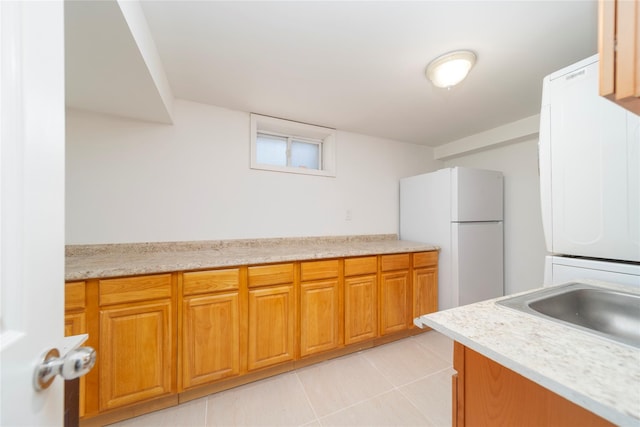 kitchen with light tile patterned floors, light countertops, brown cabinetry, freestanding refrigerator, and a sink