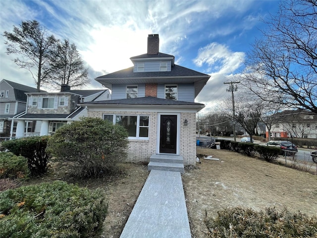 view of front of property with brick siding, a chimney, and fence