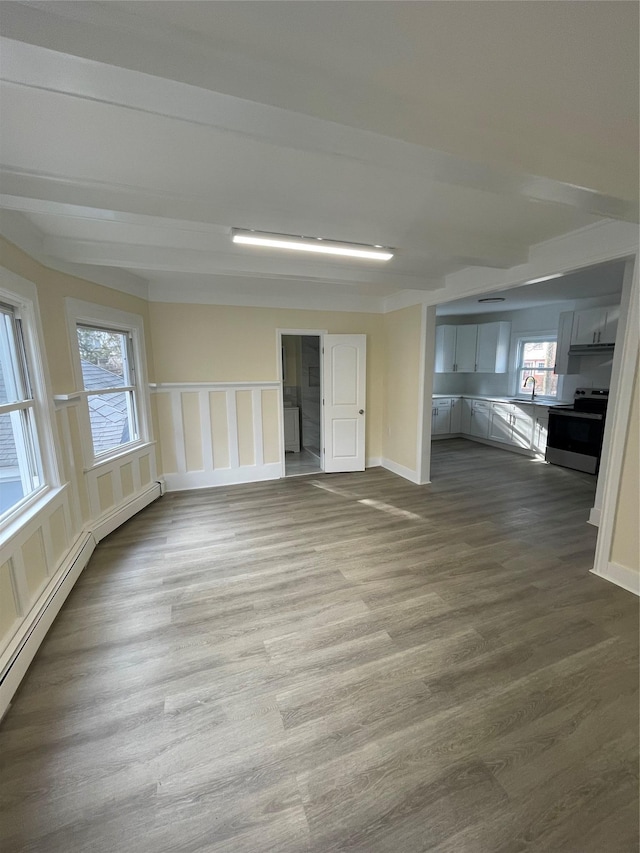 unfurnished room with a sink, a baseboard heating unit, dark wood finished floors, and baseboards