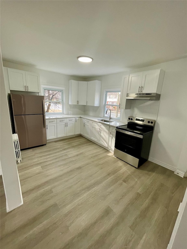 kitchen with appliances with stainless steel finishes, a sink, light wood-style flooring, and white cabinets