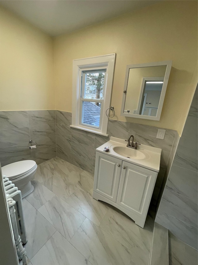 half bath with toilet, a wainscoted wall, vanity, tile walls, and marble finish floor