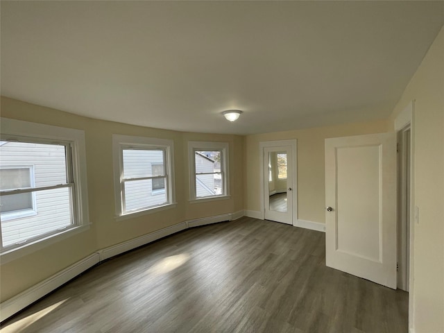 unfurnished room with dark wood-style floors, baseboard heating, baseboards, and a healthy amount of sunlight