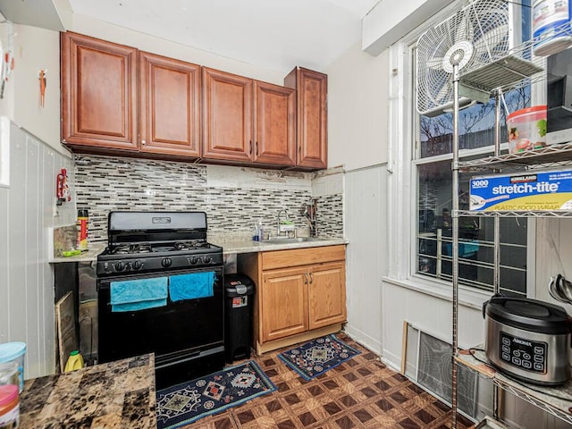 kitchen with tasteful backsplash, brown cabinetry, black gas range oven, dark floors, and a sink