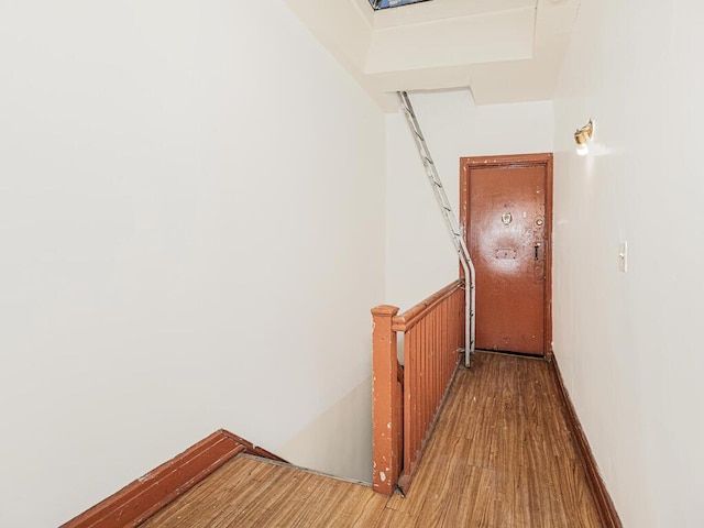 corridor with baseboards, wood finished floors, and an upstairs landing