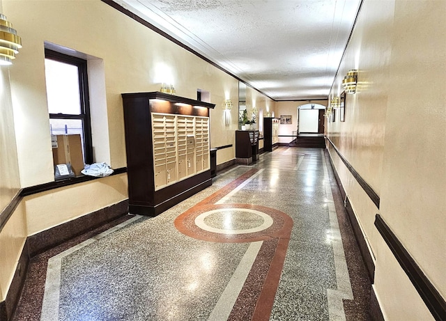 hallway featuring crown molding, mail area, baseboards, and a textured ceiling