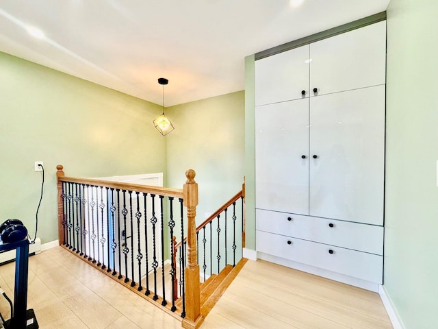 hall featuring light wood-style flooring, an upstairs landing, and baseboards