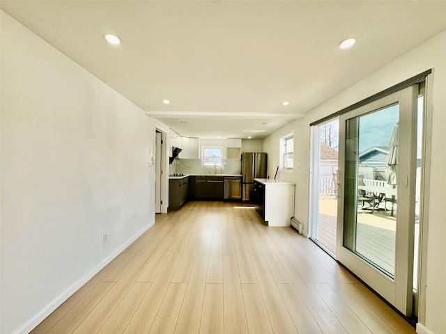 kitchen with baseboard heating, appliances with stainless steel finishes, light countertops, and light wood-style floors