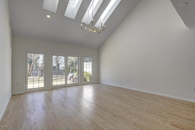 unfurnished room with high vaulted ceiling, a skylight, light wood-style flooring, and baseboards