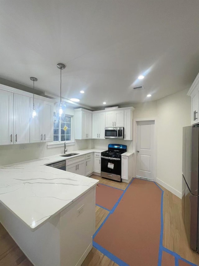 kitchen featuring visible vents, a peninsula, stainless steel appliances, white cabinetry, and a sink